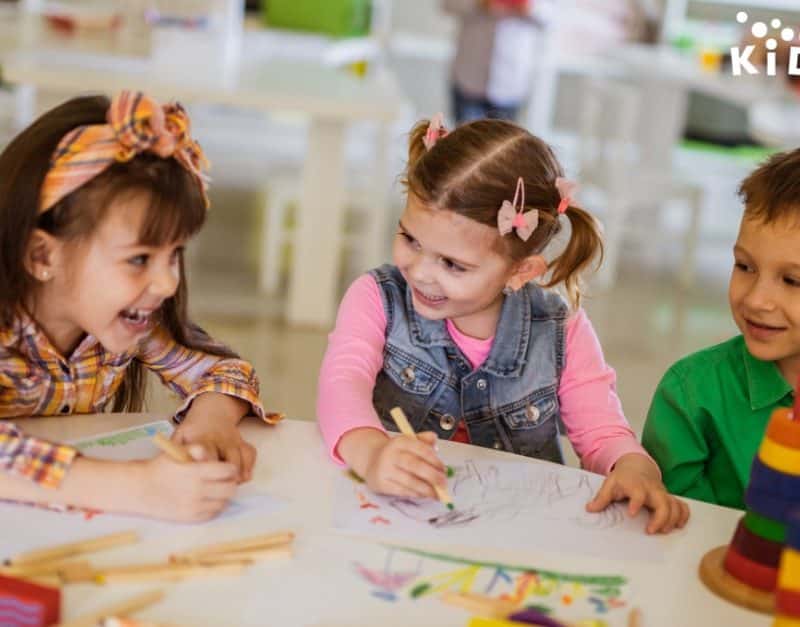3 children in Sacramento CA smiling and coloring at table at KidsPark.